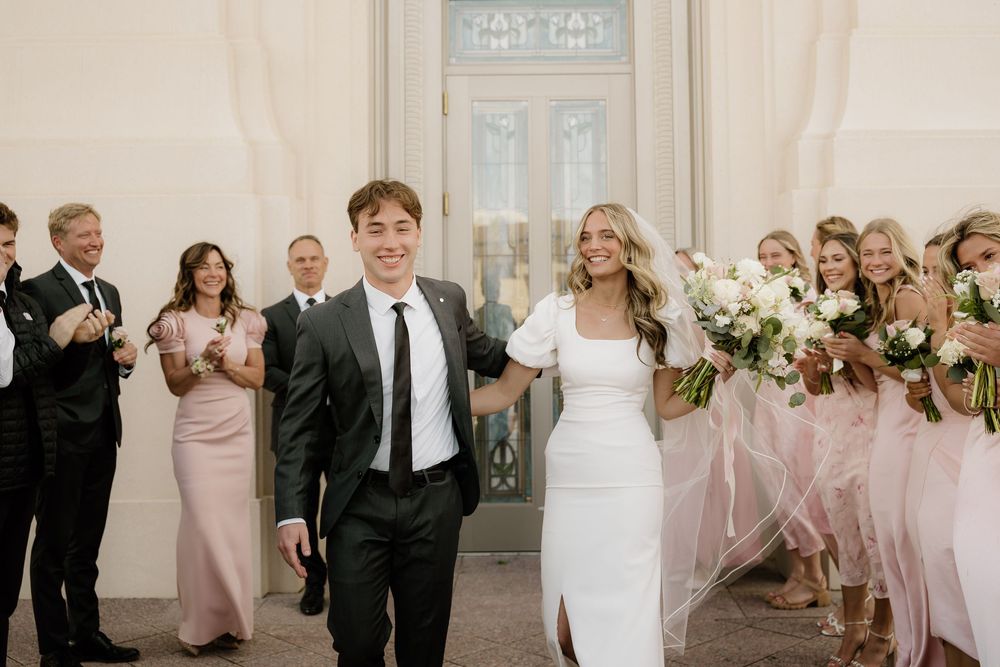 Newlyweds exit ceremony while wedding party in blush pink dresses applauds along church doorway.