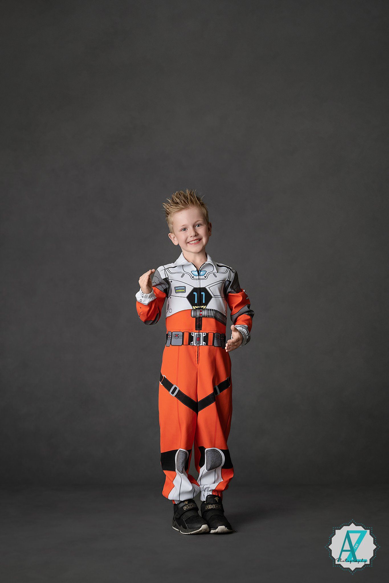 A young child wearing an orange and white space suit costume poses against a dark grey background.