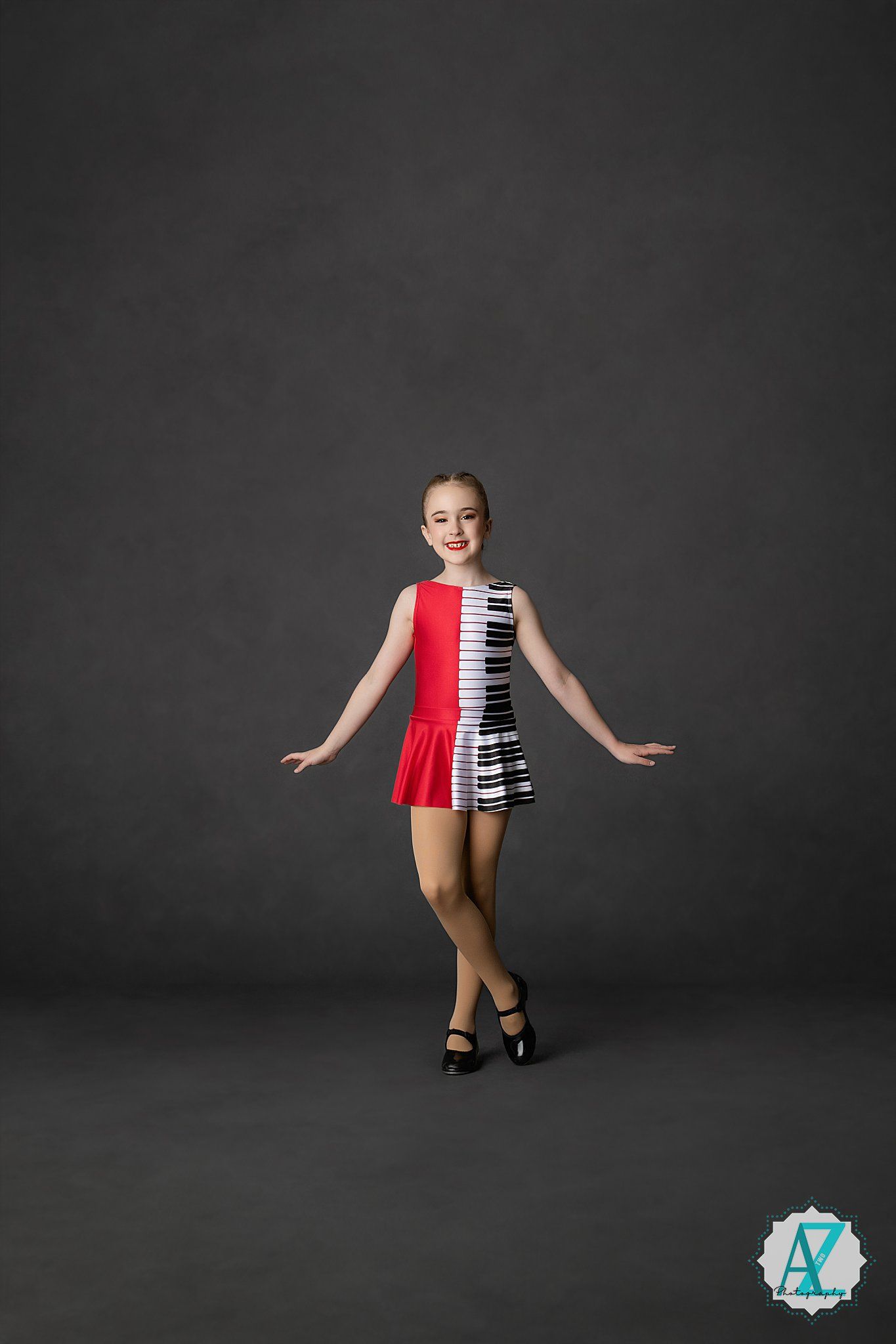 Performer in red and black piano key patterned dance costume poses elegantly against dark backdrop.