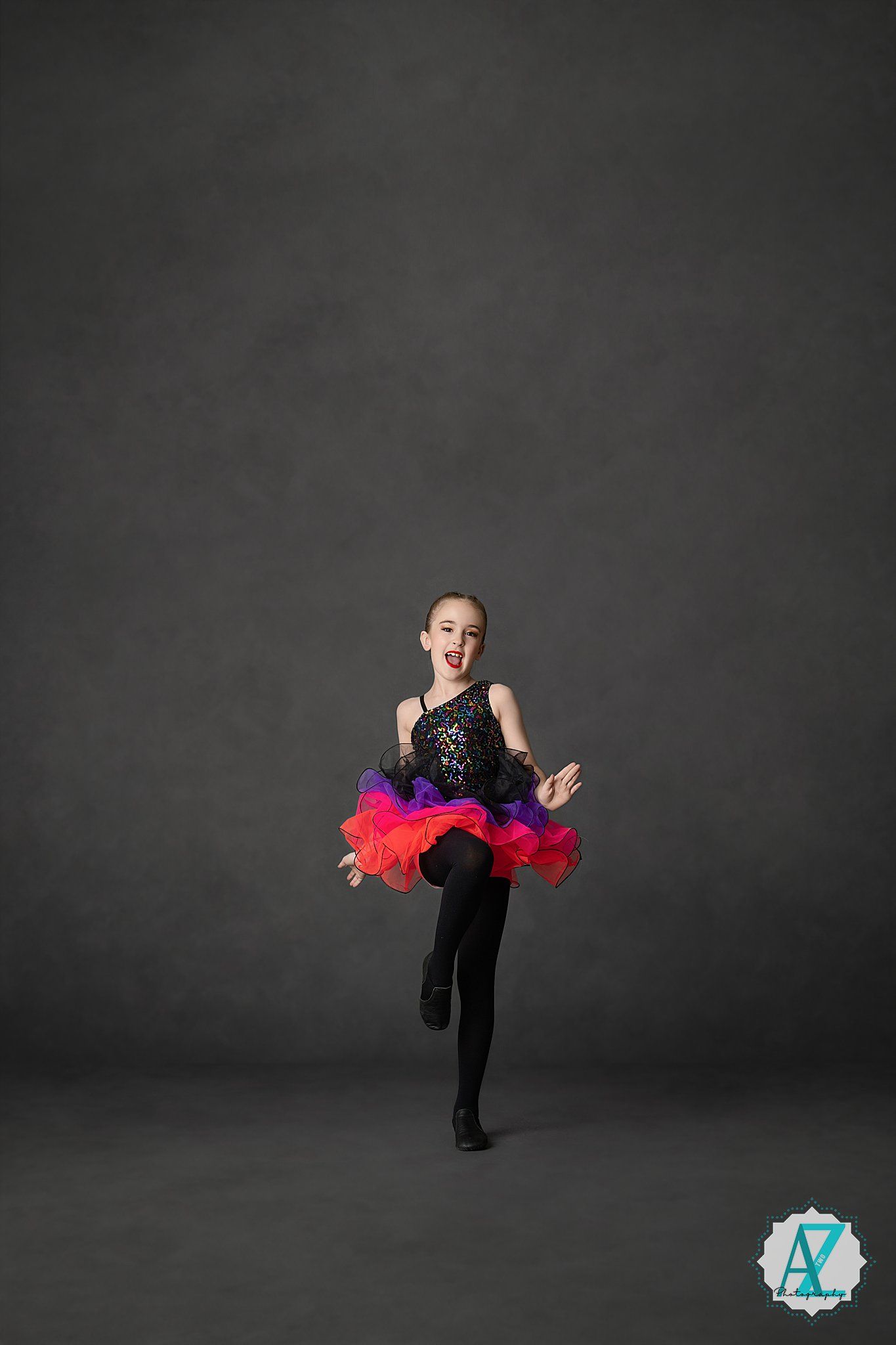 A dancer in a black and red tutu performs an elegant pose against a dark gray studio backdrop.