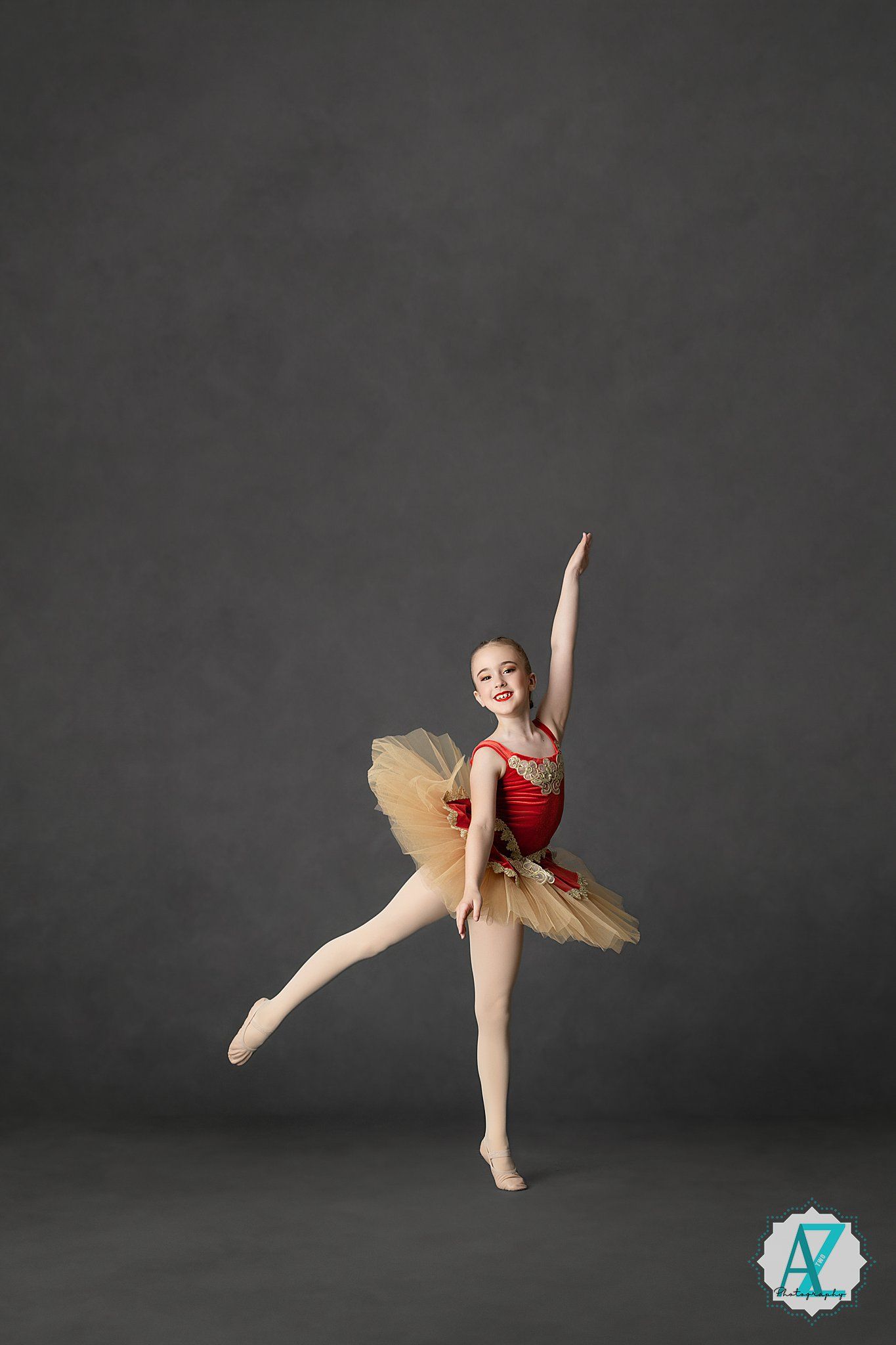Ballet dancer in gold and red tutu performs elegant dance poses against dark studio backdrop.