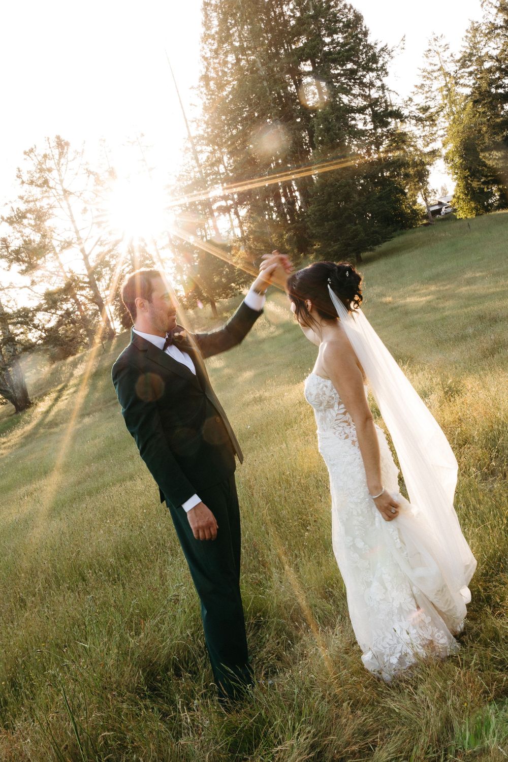 Bride and groom dancing outdoors in golden sunset light, surrounded by lush green trees on their wedding day.