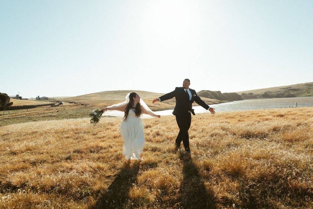 A couple walks hand in hand through a golden field at sunset during a romantic outdoor photography session.