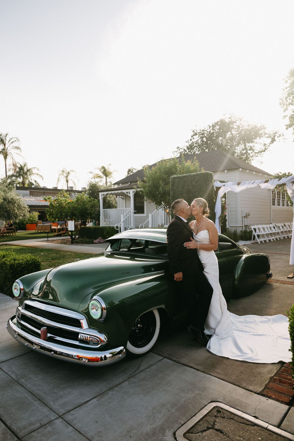 A vintage green Chevrolet classic car parked outside a white building with palm trees in the background at dusk.