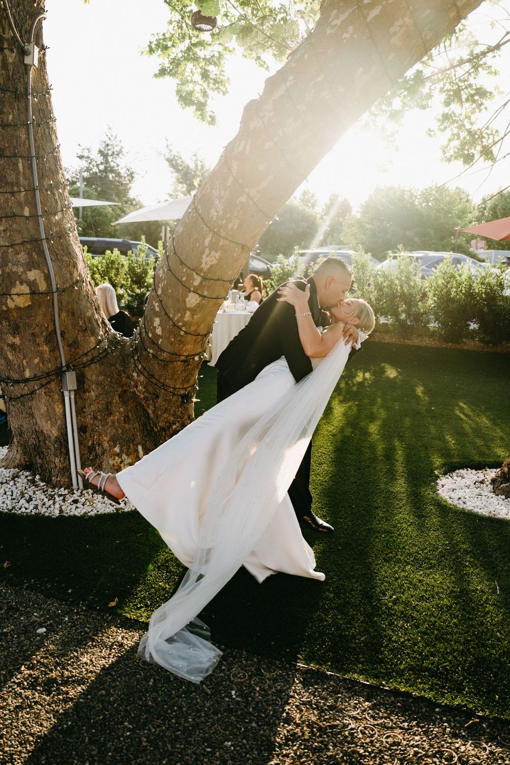A romantic dip pose with a couple embracing under a tree at sunset during a wedding in an outdoor garden setting.