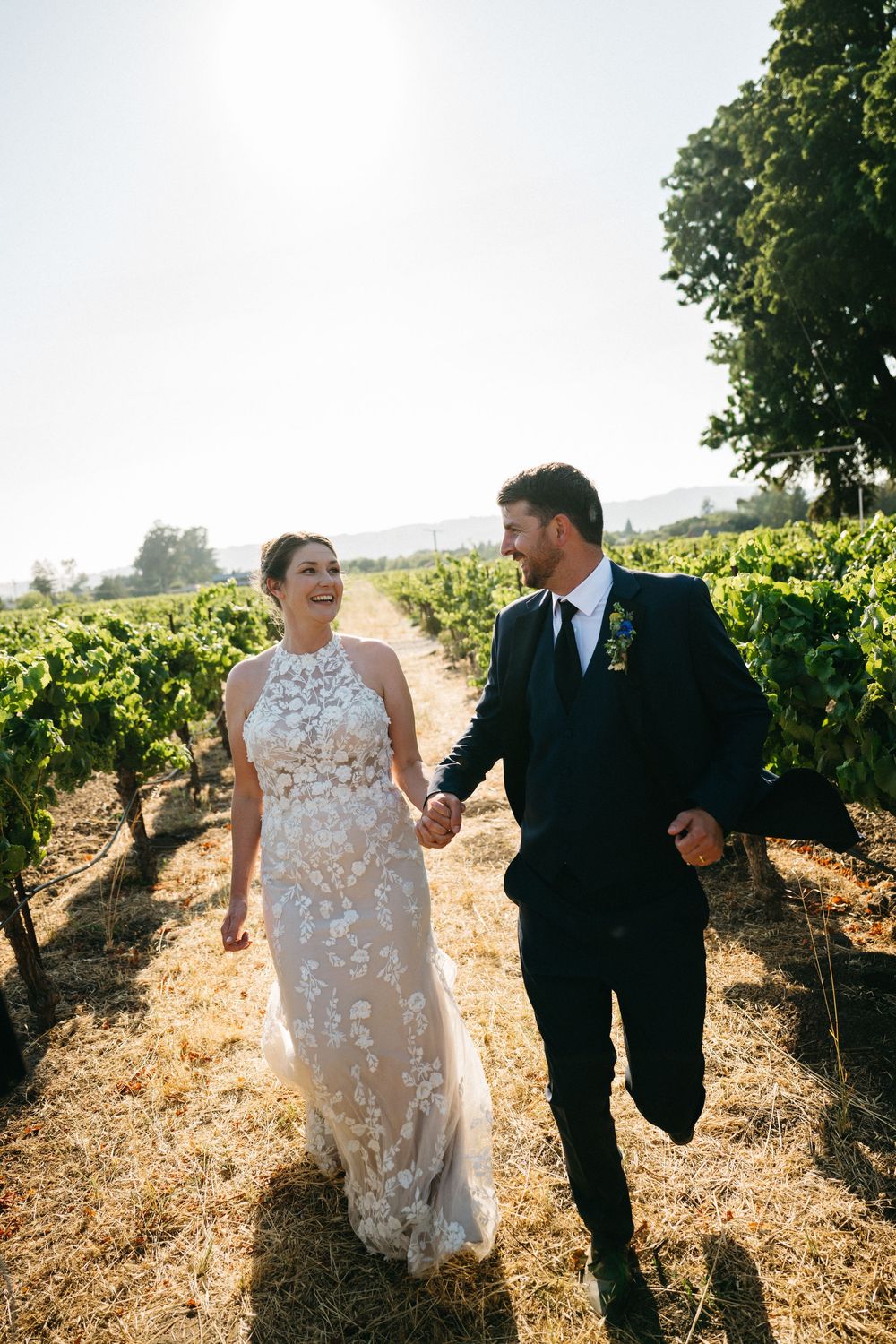 Couple walking hand in hand through scenic vineyard rows on a sunny summer day in Sonoma County, CA