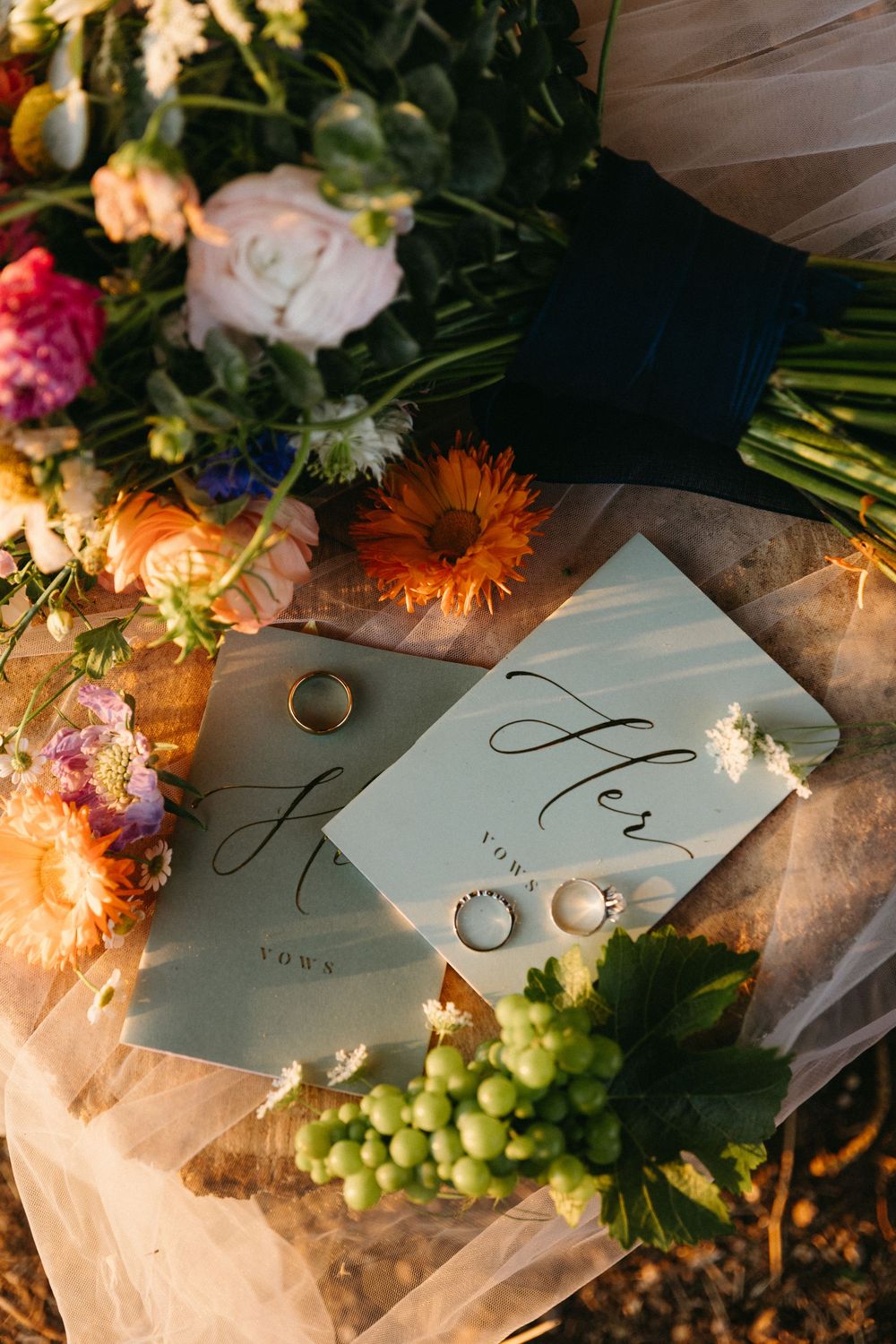 Wedding flat lay with his and her vow books, and colorful flowers arranged with wedding rings in natural light in Healdsburg, CA