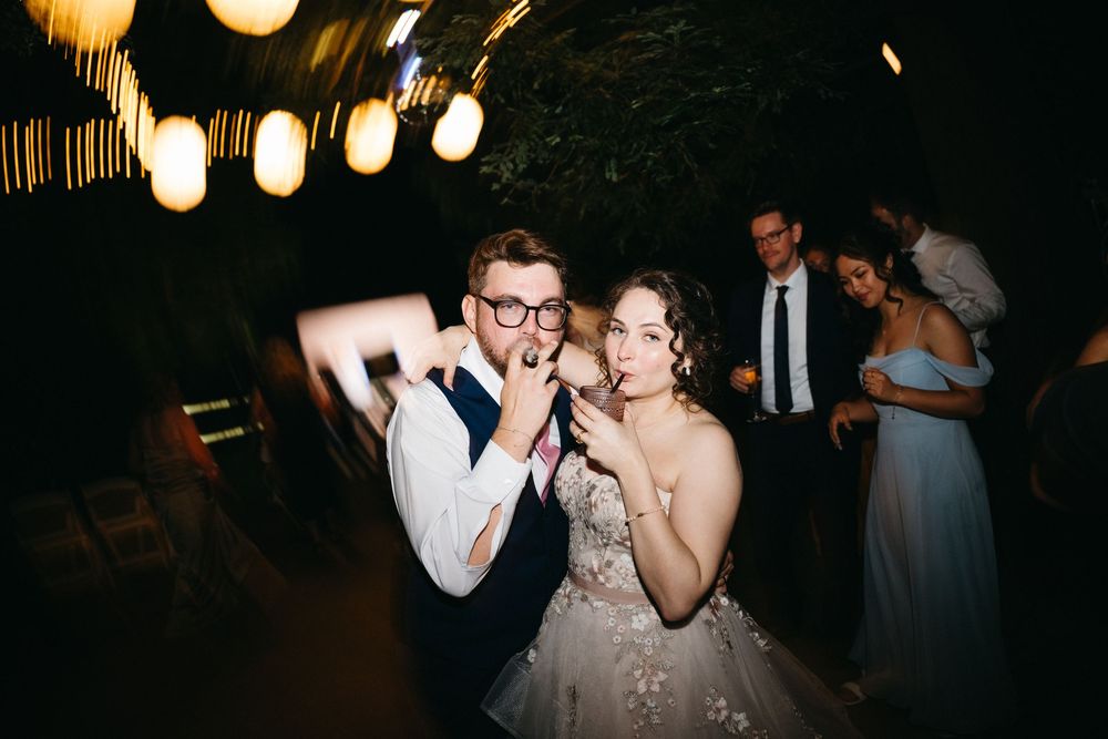 Bride and groom dancing and laughing together at their wedding reception with guests celebrating in the background.