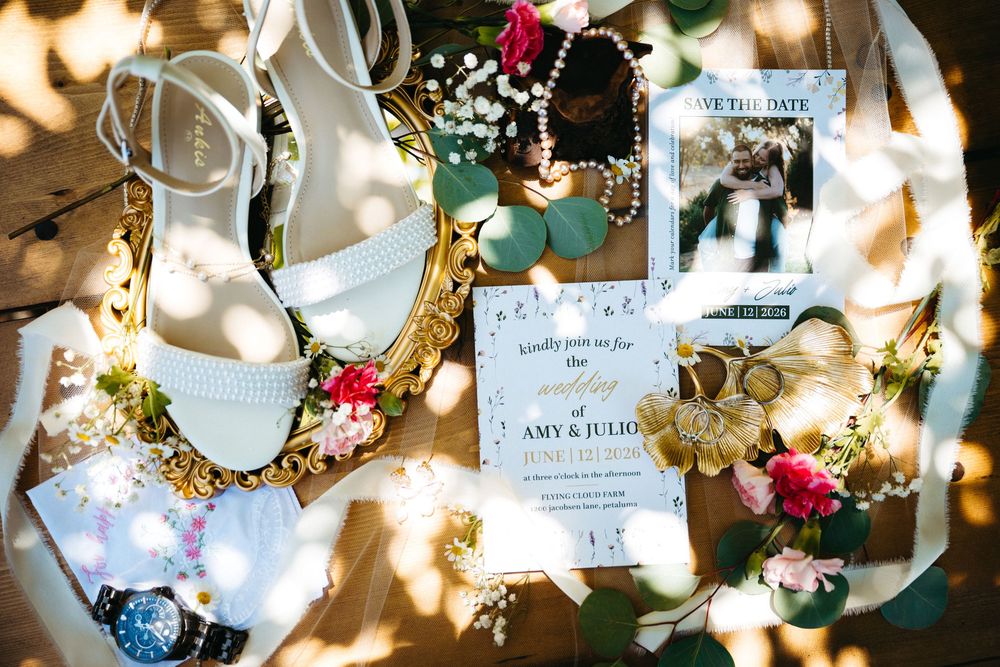 Wedding flat lay featuring white heels, save the date card for Amy and Julio, floral accessories, jewelry, and a vintage gold mirror.