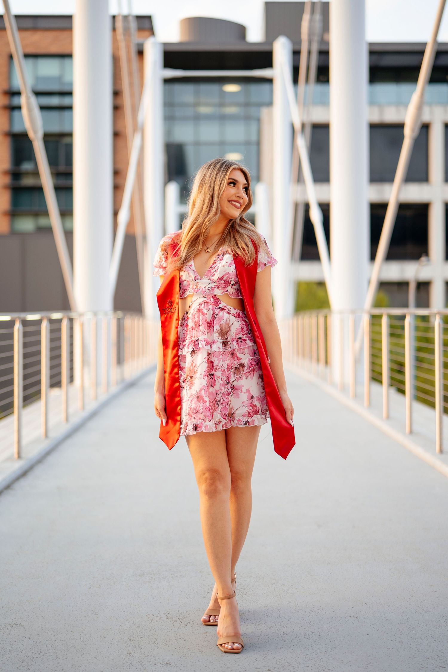 Woman in a white summer dress with colorful sun and floral prints poses outdoors during golden hour sunset.
