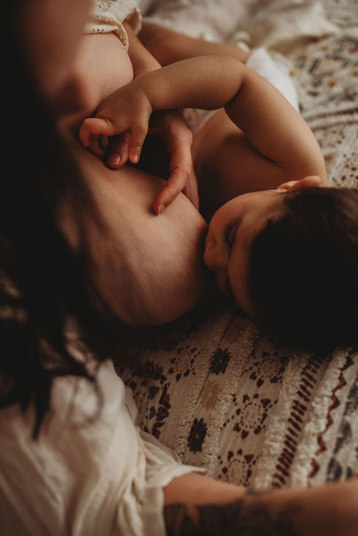 Intimate close-up photo of a nursing baby against a lace textured blanket in warm lighting.