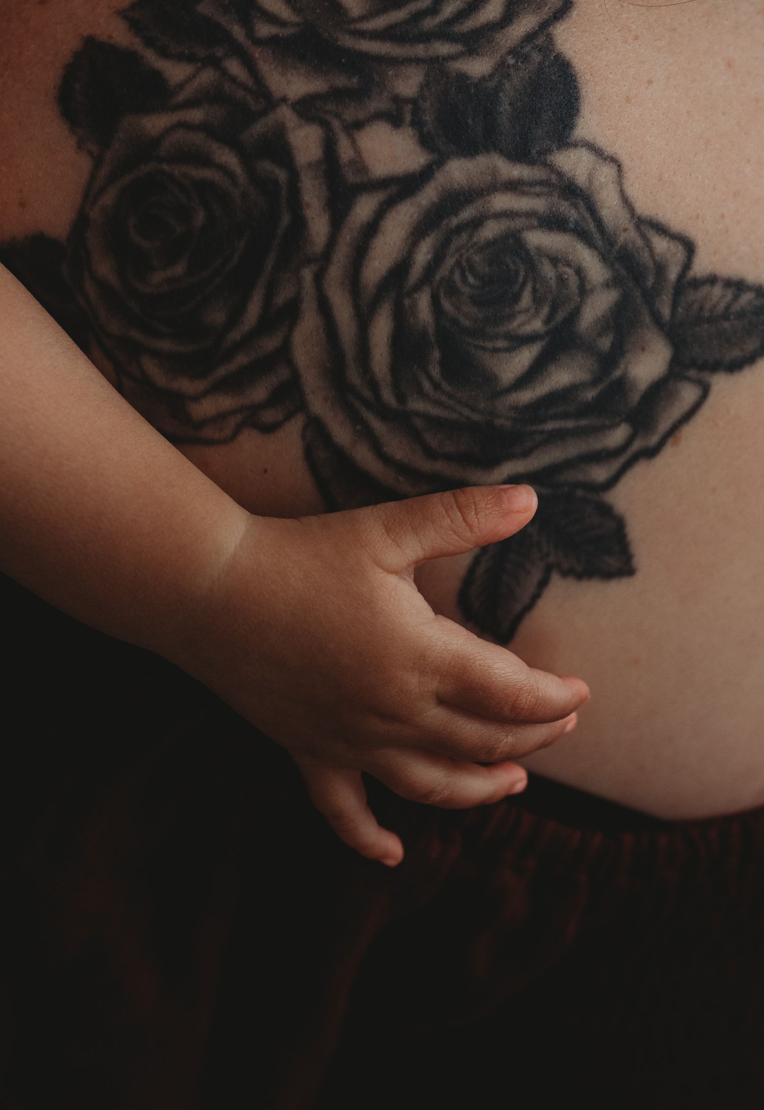 Close-up detail of rose tattoo artwork with small hand reaching across.