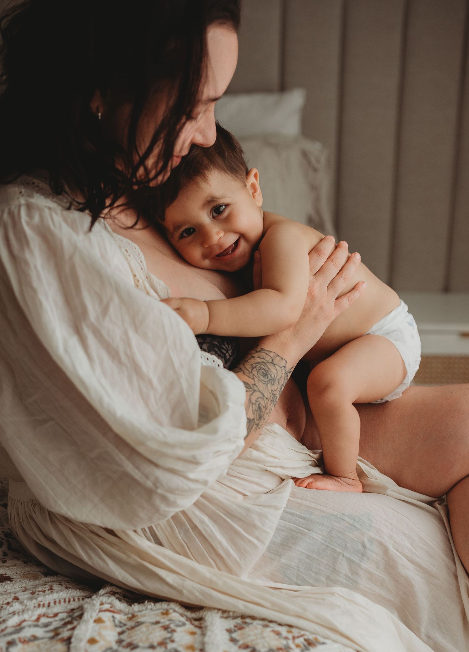 Intimate nursing photography with soft white fabric and natural lighting.