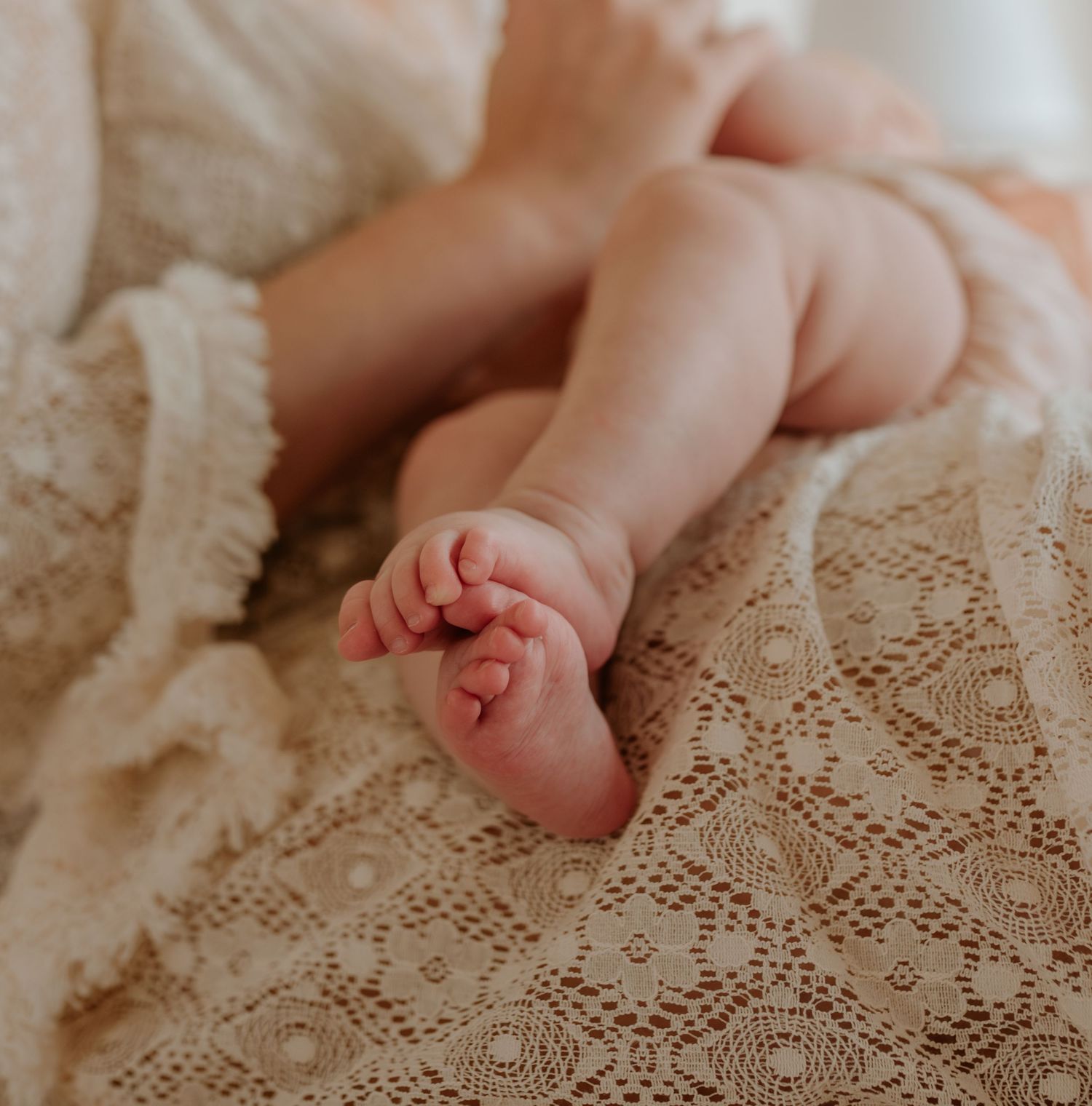 Close-up of tiny baby feet resting on vintage lace fabric.