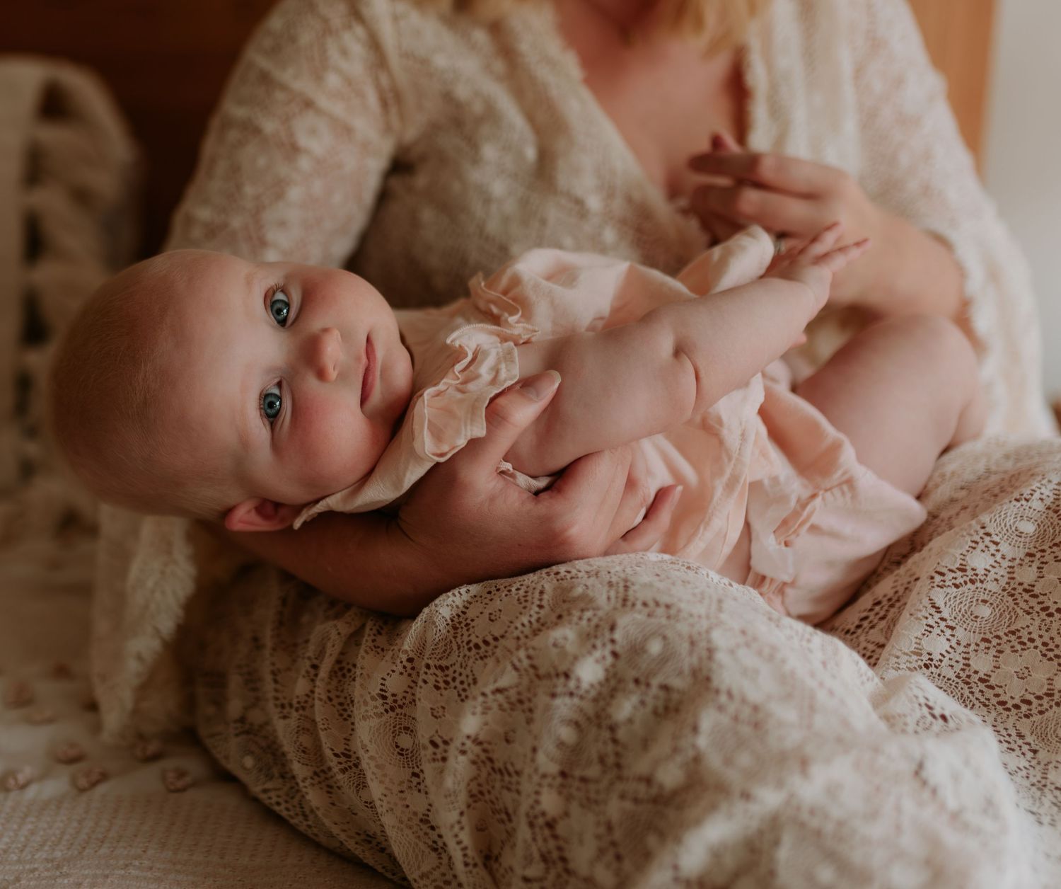 Intimate nursing moment captured in soft muted tones on white bedding.