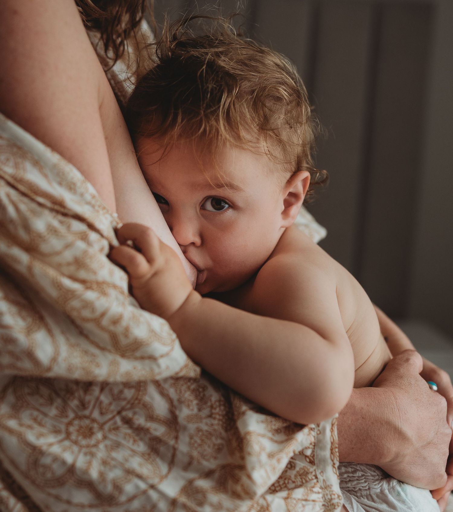 Intimate nursing moment captured in warm, moody lighting.