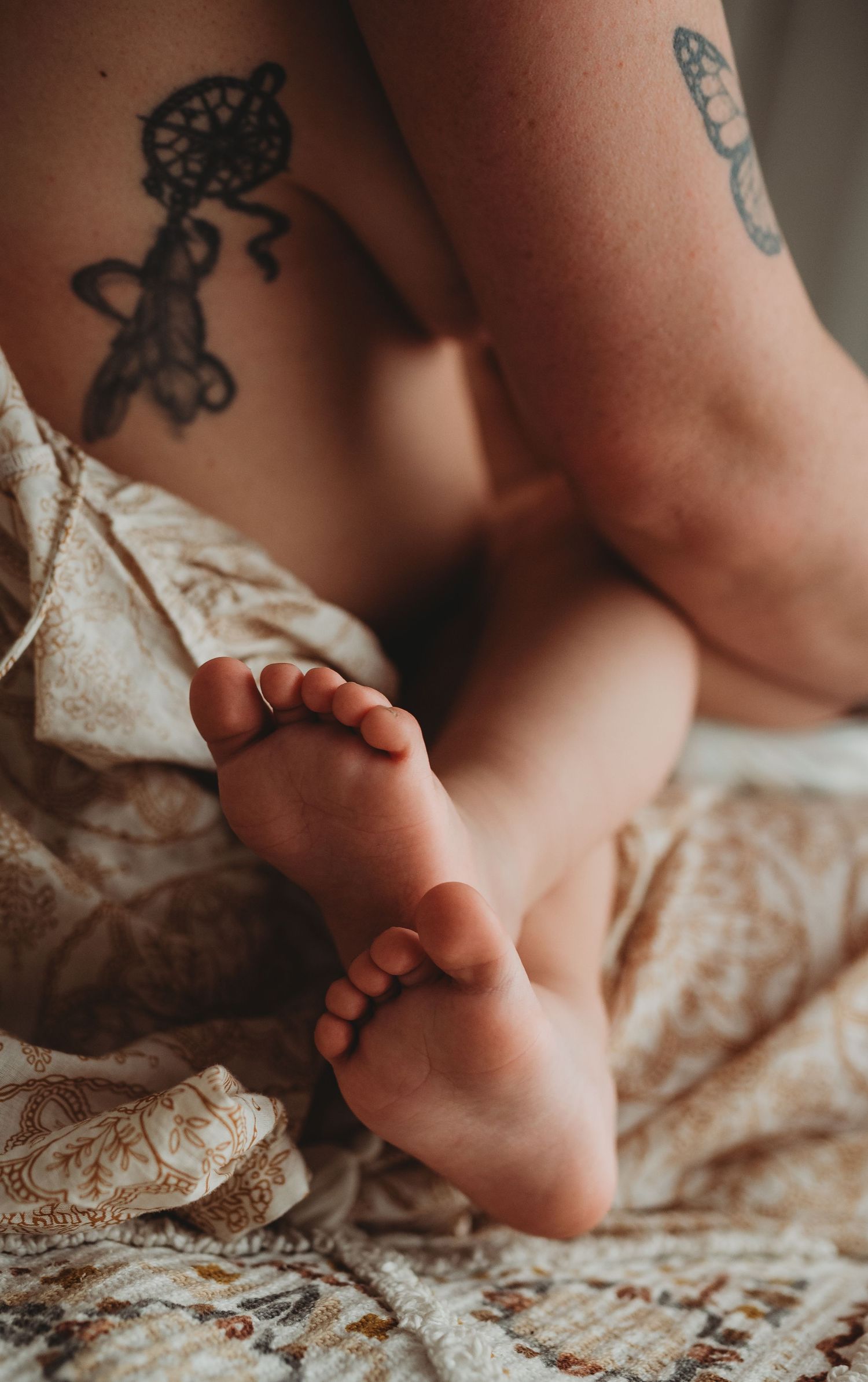 Small bare feet rest on cream colored patterned bedding in soft natural light.