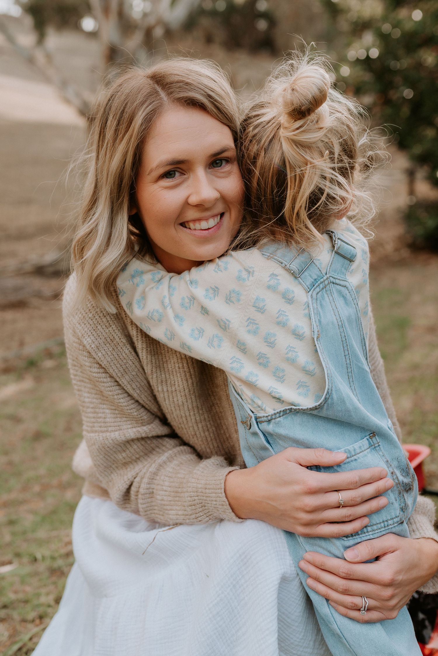 Sweet embrace captured outdoors with soft natural lighting and neutral colored clothing.