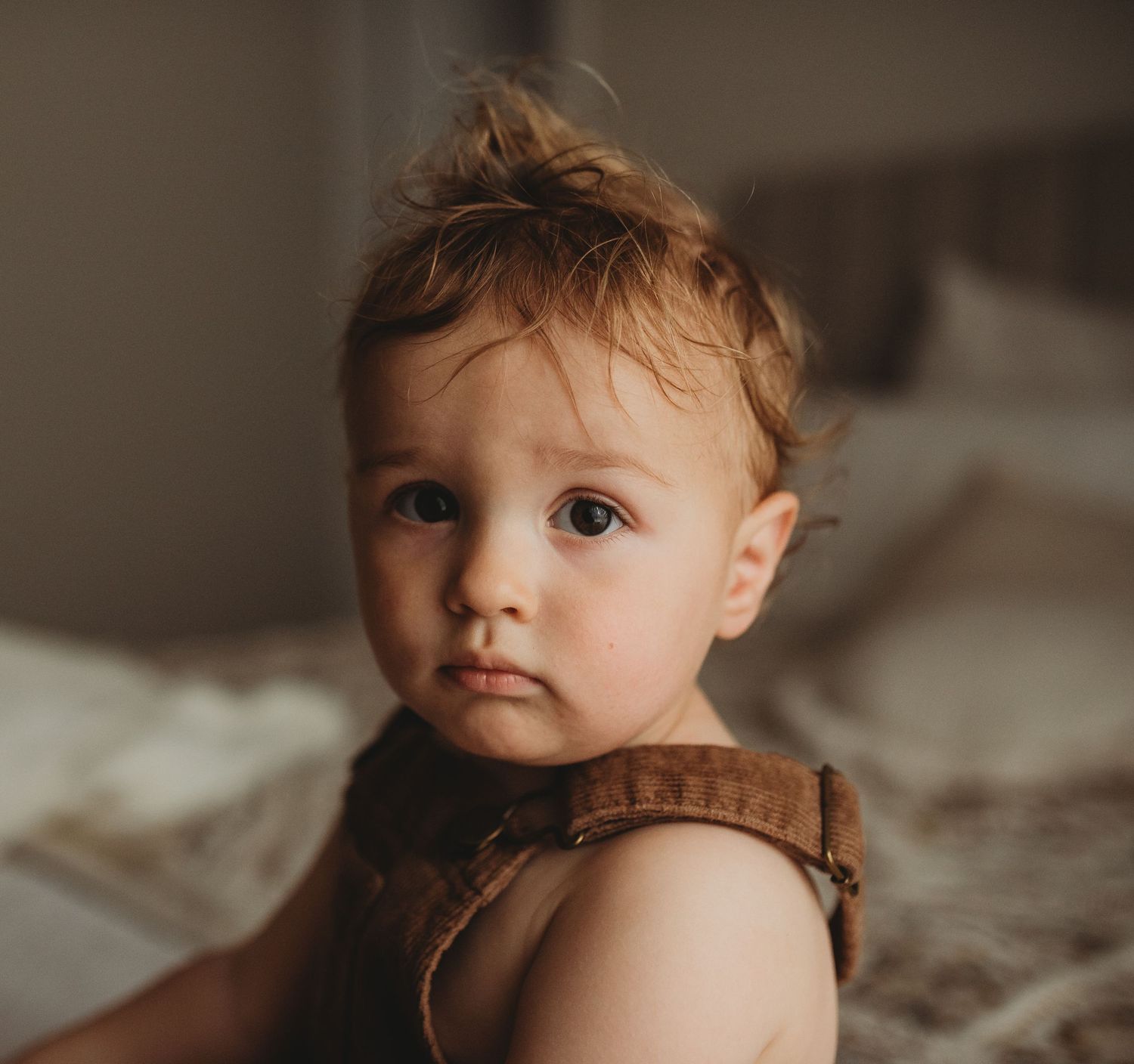 Close up portrait of a toddler with messy hair wearing a brown romper.