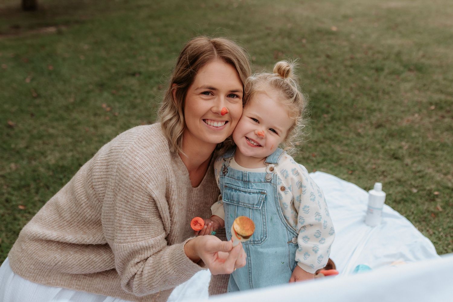 A sweet outdoor photo shoot with a beige sweater and white dress against a grassy background.