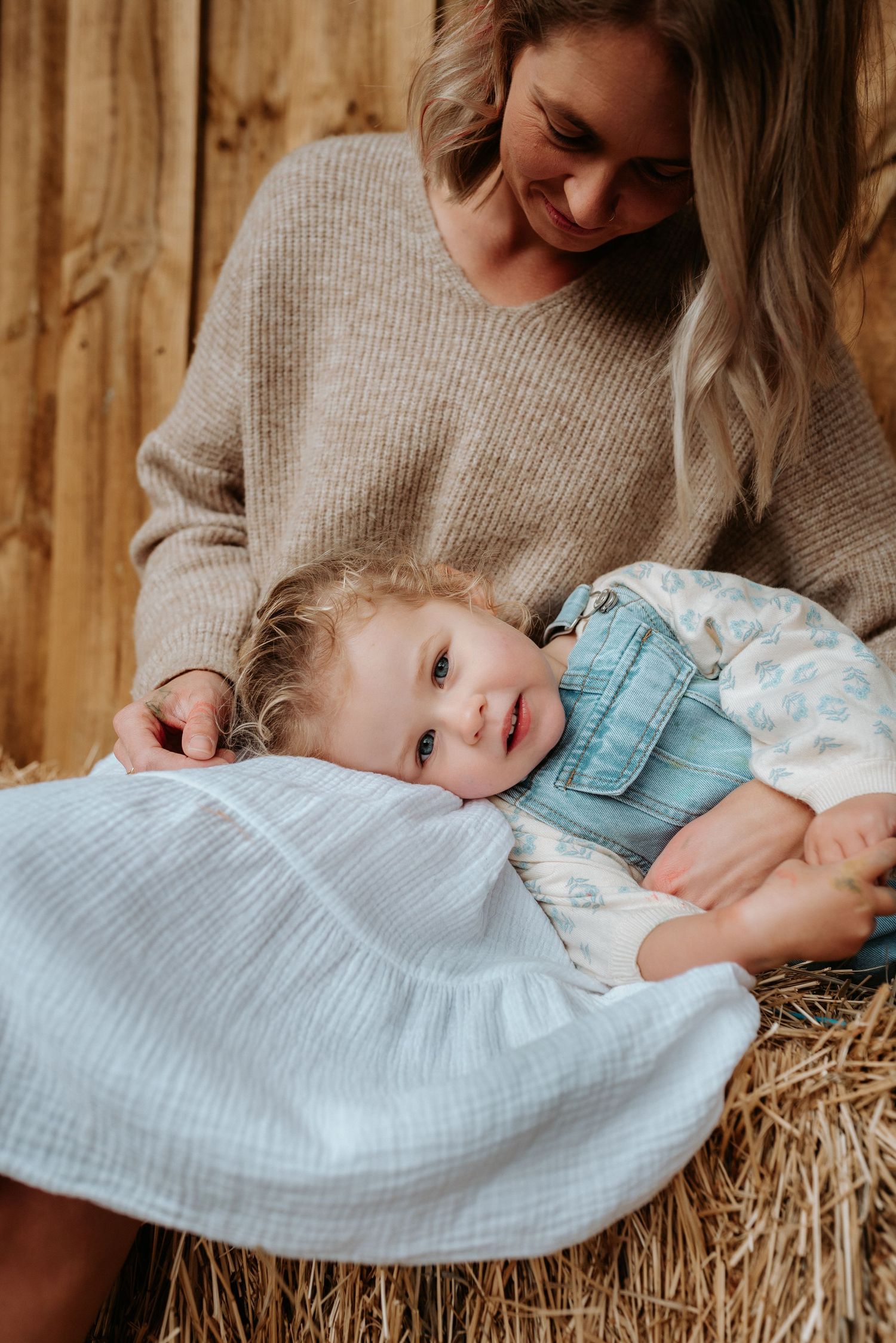Tender moment shared on hay bales with natural lighting and rustic wooden backdrop.