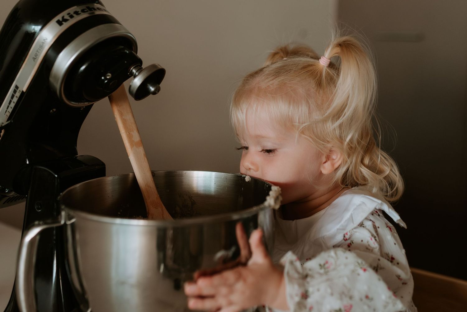 A small child reaches up to help with a black stand mixer in the kitchen.