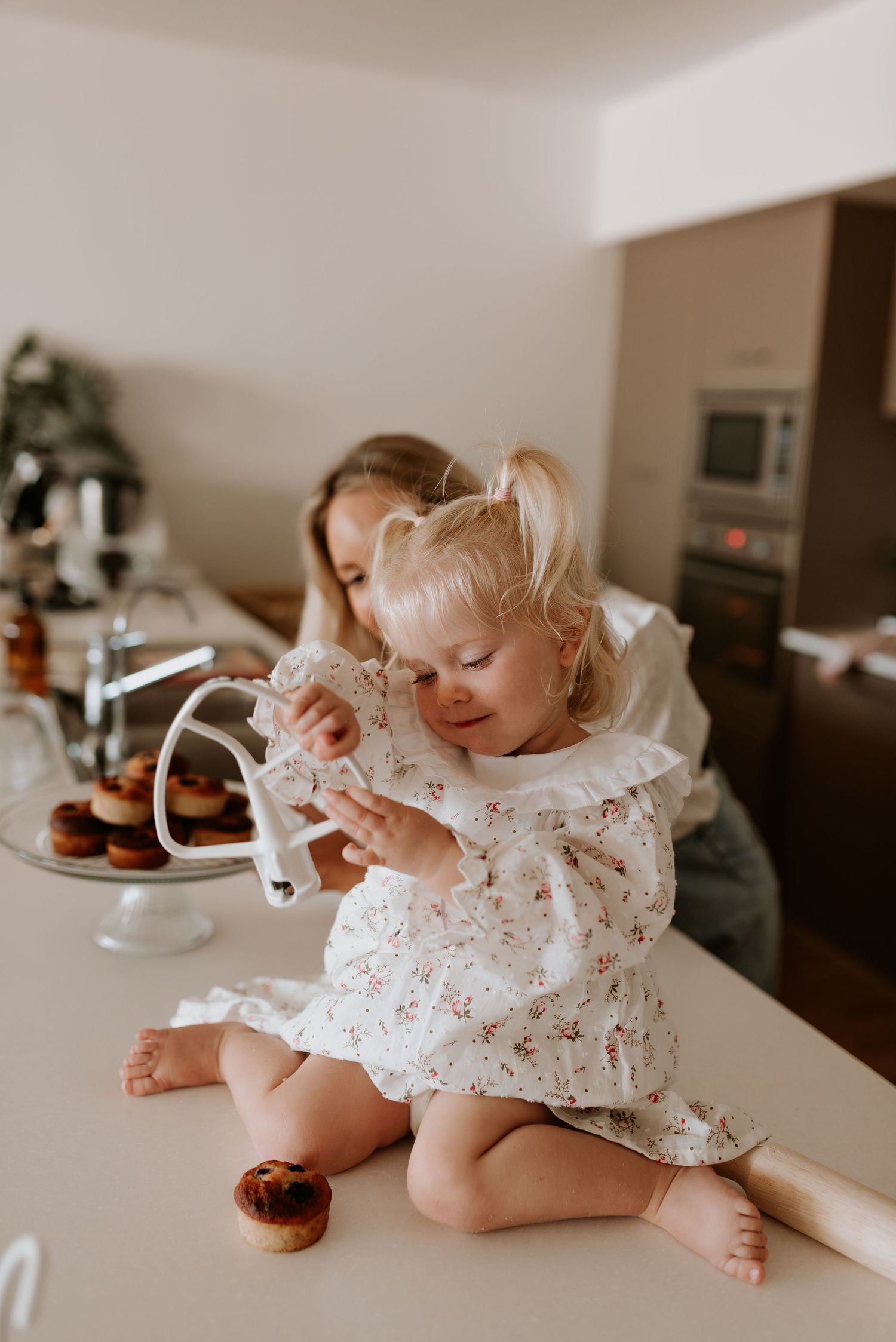A small child in a floral dress reaches for a cupcake on a counter.
