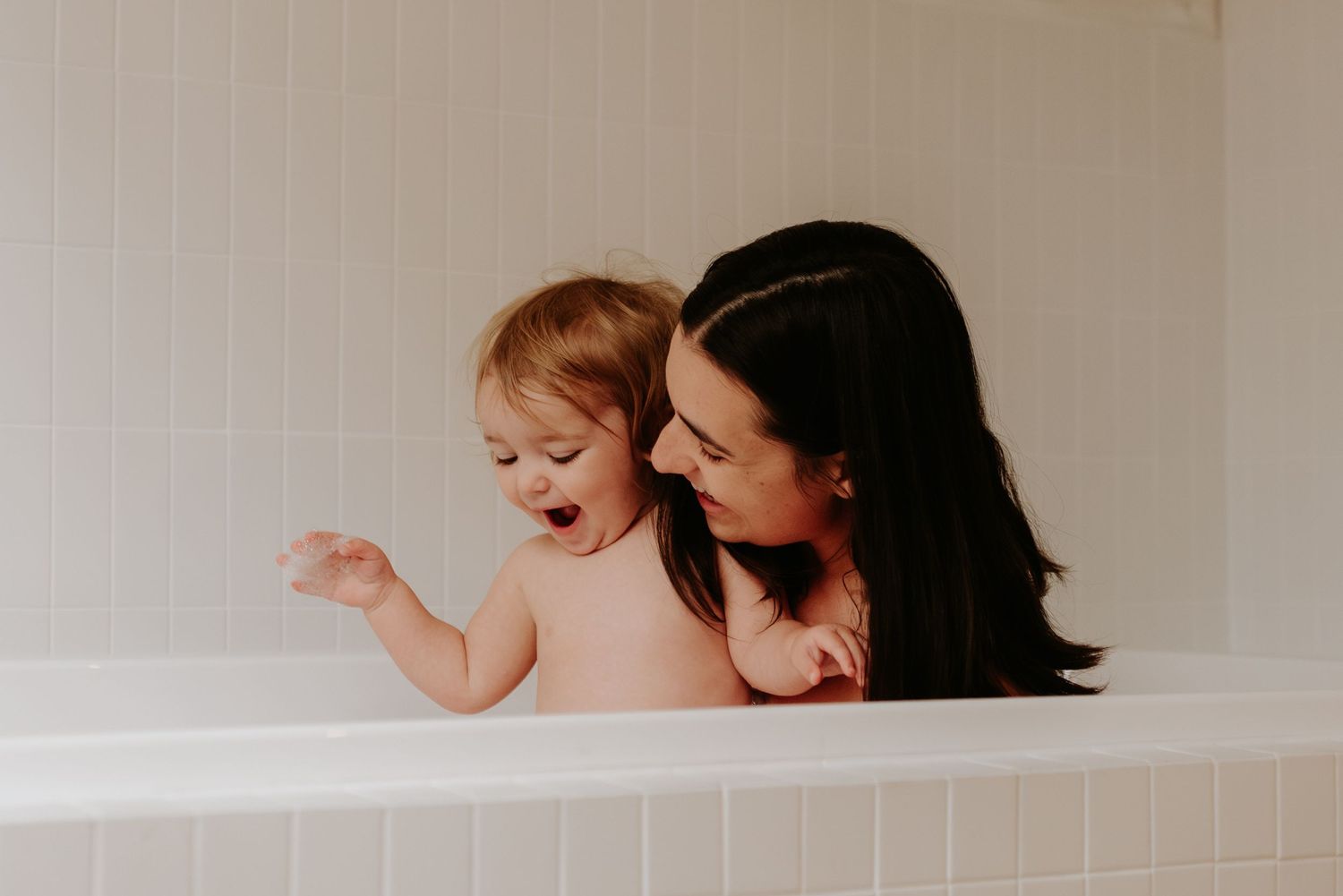 Intimate bathtub scene showing tender bonding moment between parent and baby in natural light.