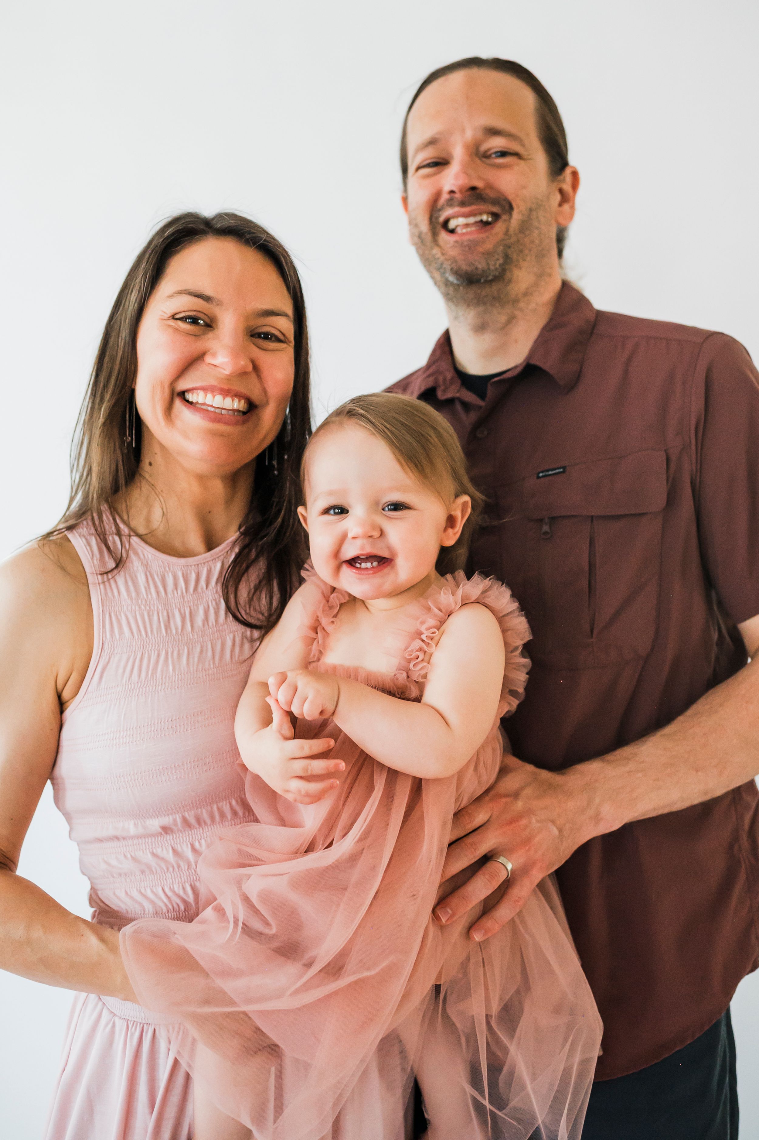 A family poses together against a white backdrop wearing coordinated pink and brown outfits.