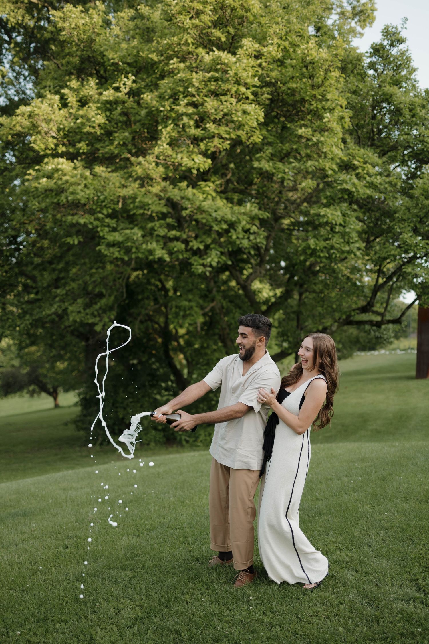 A couple sharing a sweet proposal moment under a tree while friends watch in the background at sunset.