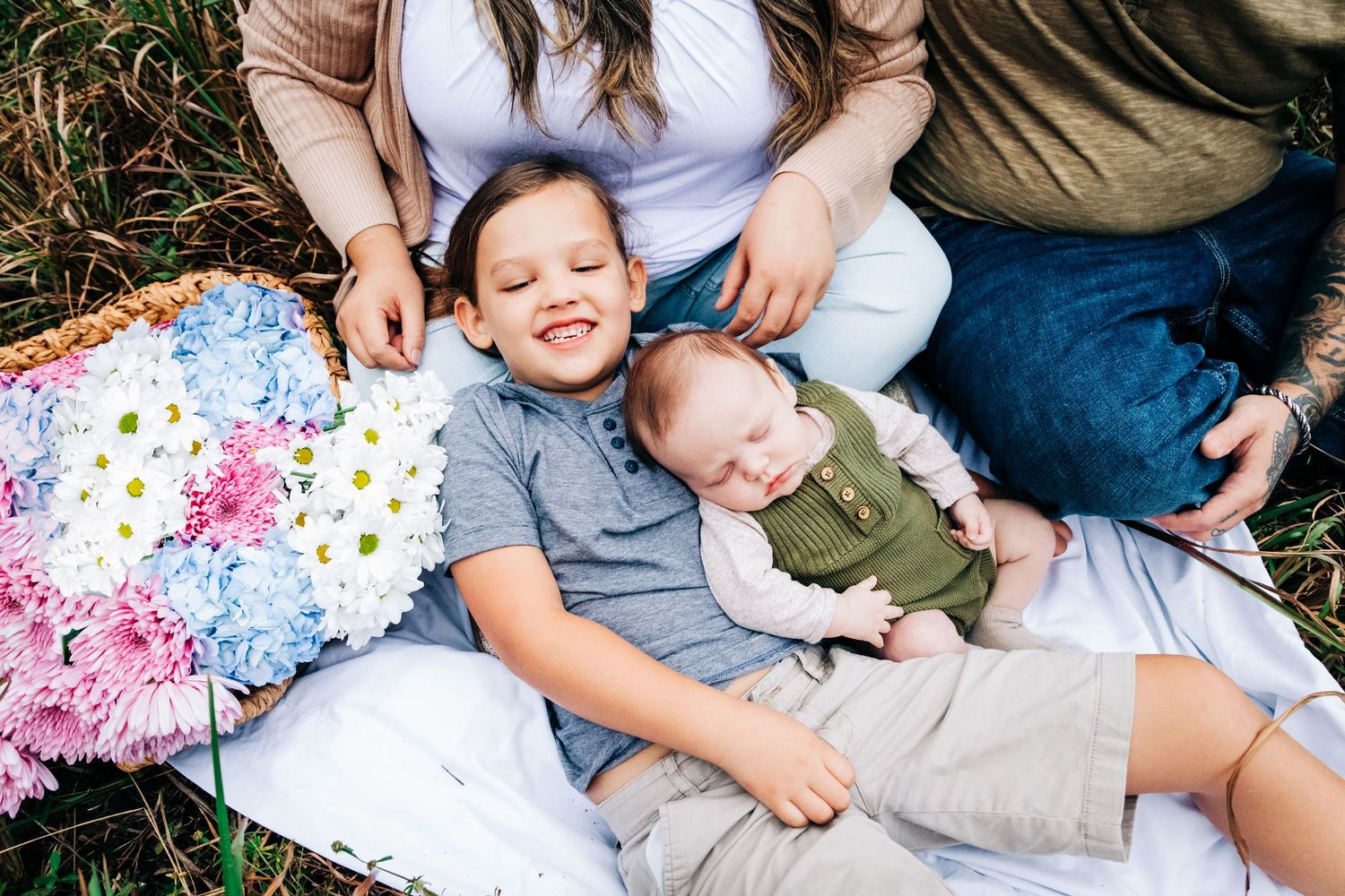 Family relaxes together on a blanket outdoors with colorful floral fabric and casual clothing at riverbend park in Jupiter fl.