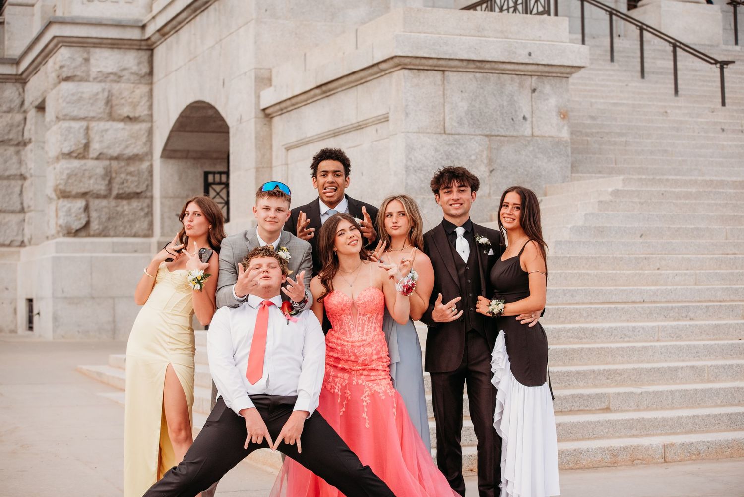 Group of young people in formal attire pose on stone steps outside building for special occasion photo.