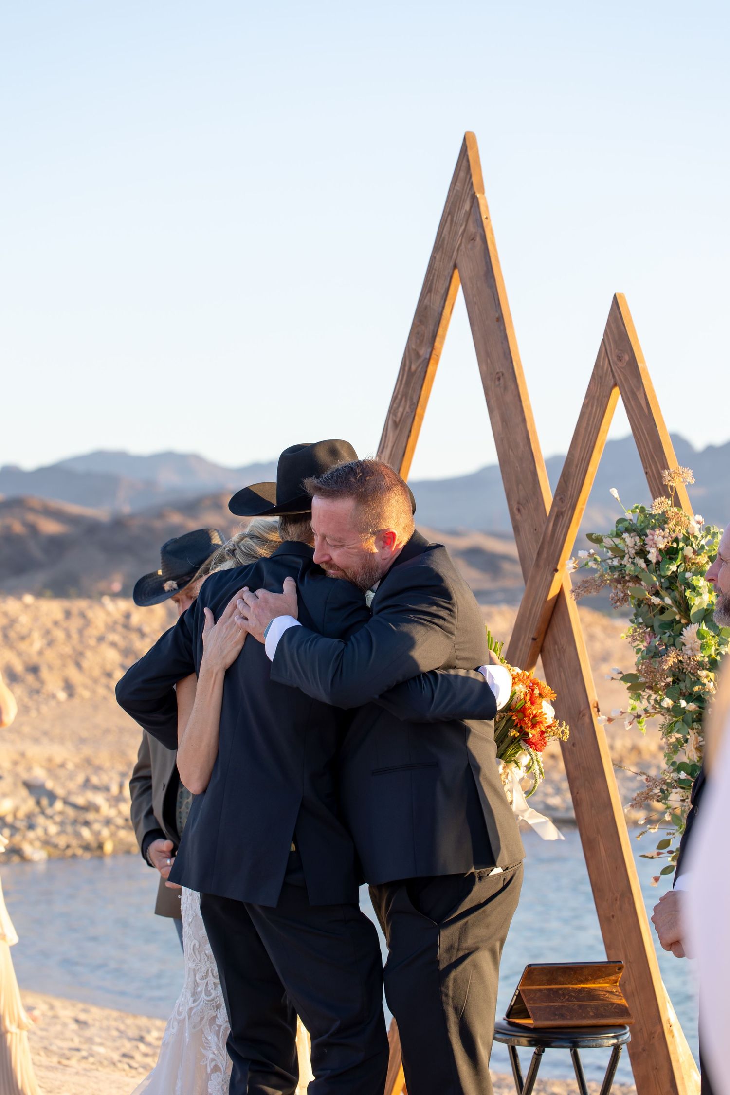 Wedding ceremony on a beach with triangular wooden arch structure decorated with flowers at sunset.