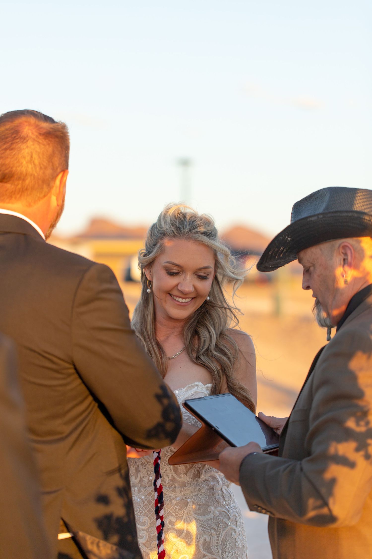A wedding ceremony takes place at sunset with an officiant reading from a book during an outdoor desert ceremony.