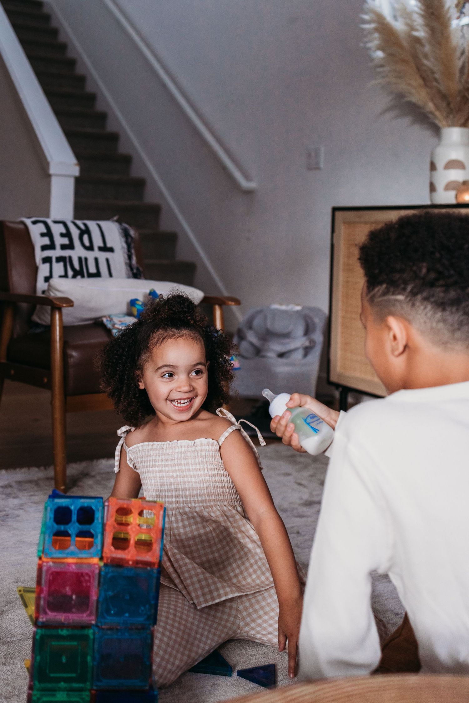 Young child and adult playing together with colorful magnetic building blocks on a carpeted floor at home.