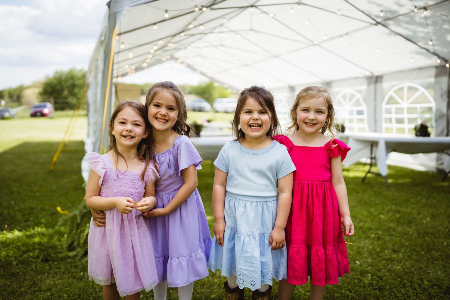 A group of children in colorful dresses standing together outdoors at what appears to be a summer event.