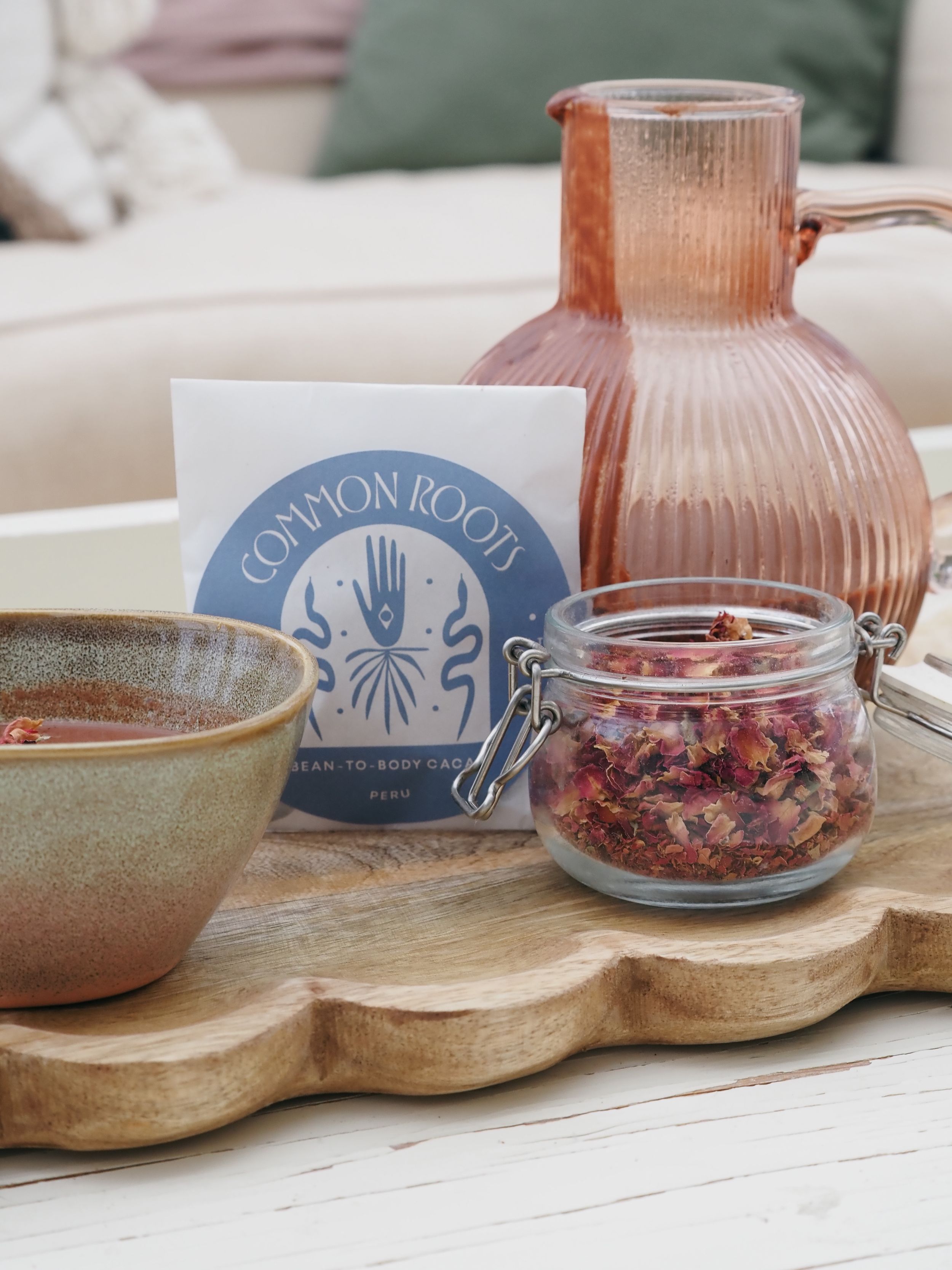 Pink textured glass carafe on wooden board with rustic bowl and jar of dried flowers next to Common Room branding.