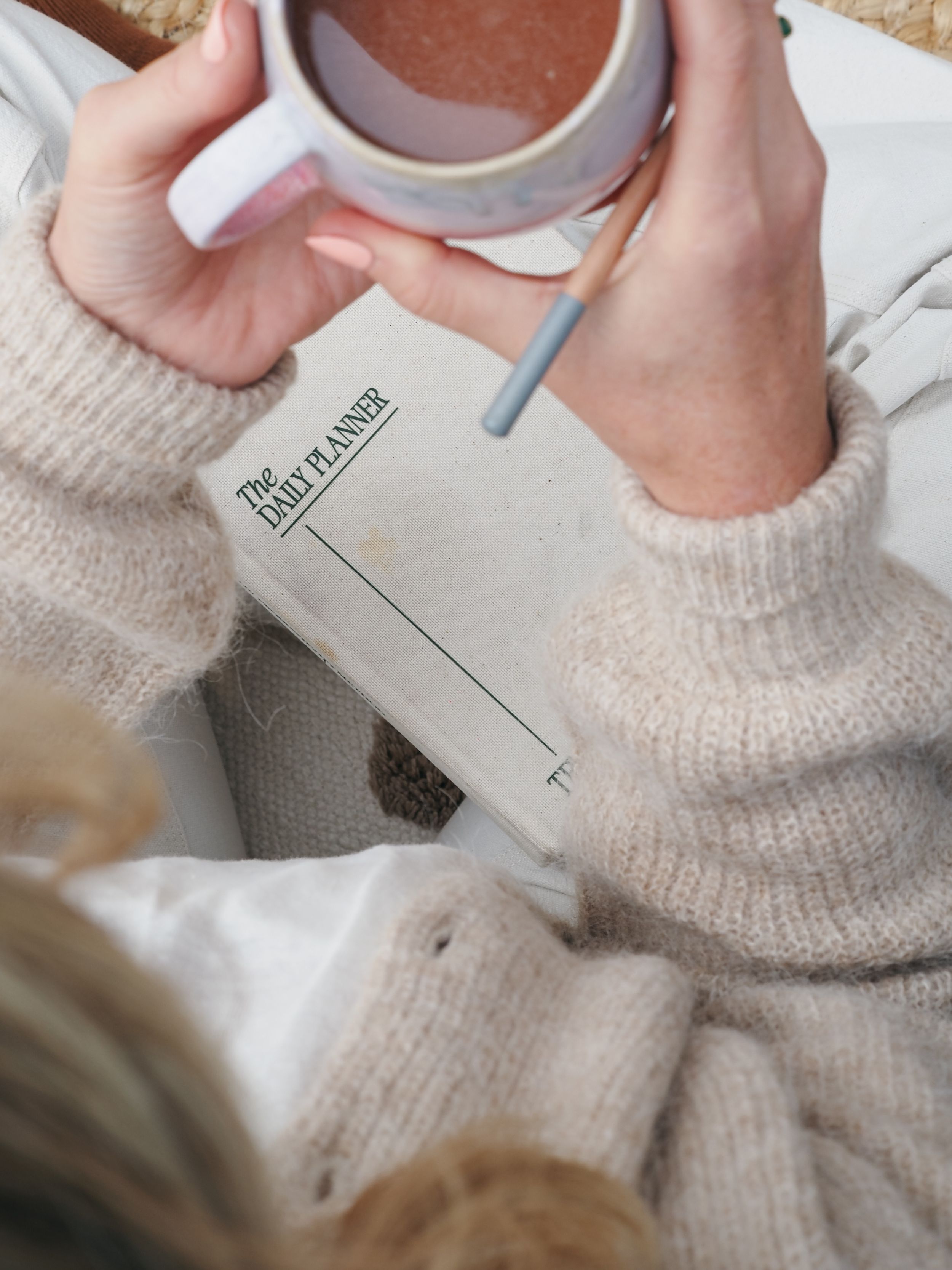 Person in cozy cream sweater reading a book while holding a warm beverage in a white mug.