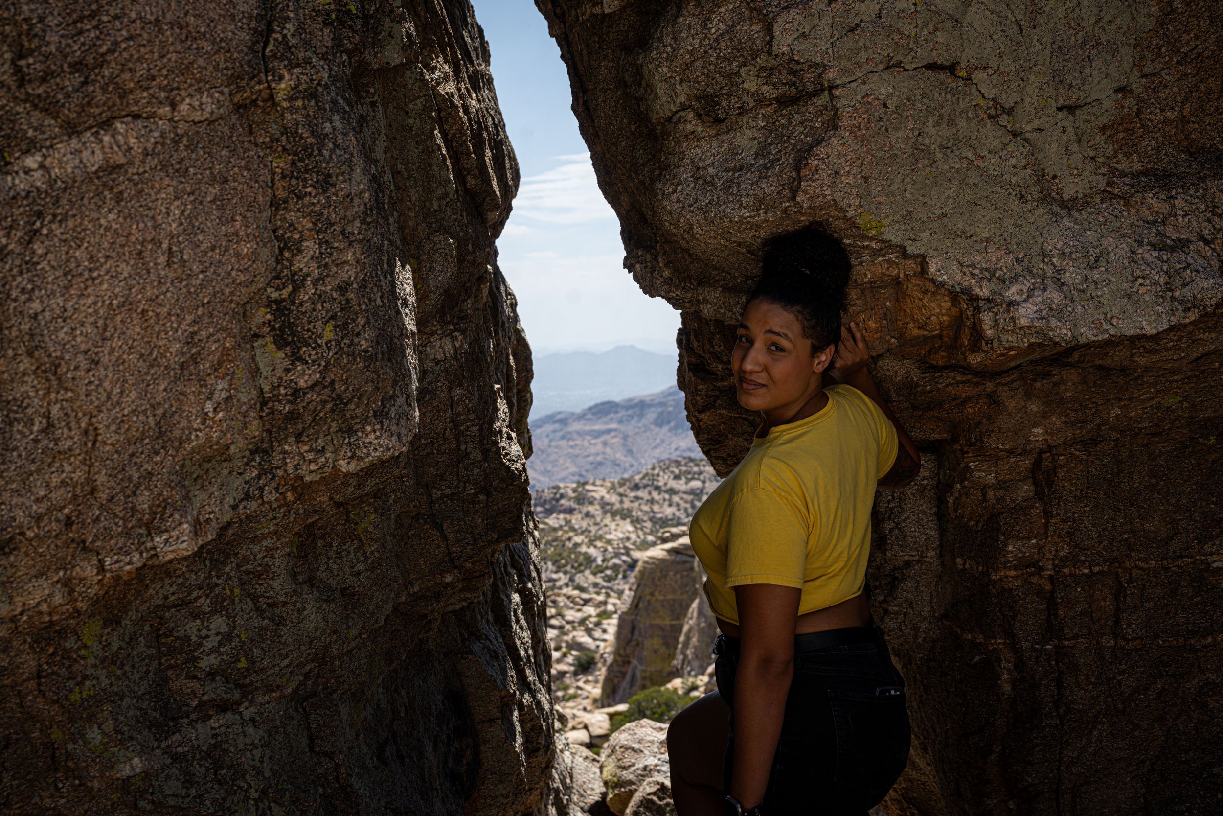 Person exploring cave entrance with desert valley views through rocky opening.
