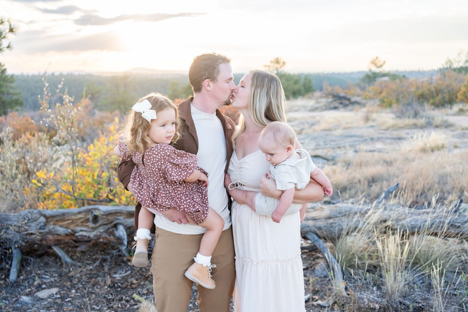 Family in matching neutral outfits embracing in a desert landscape with golden sunlight and autumn foliage.