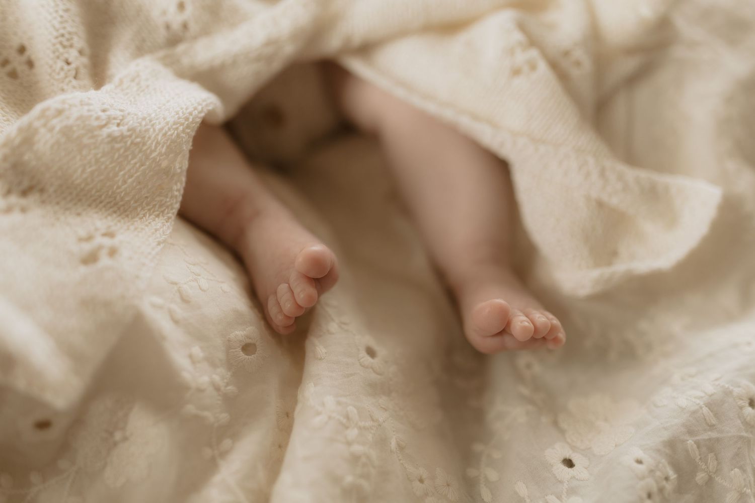 Close up of hands tenderly touching a pregnant belly draped in cream colored fabric in soft natural light.