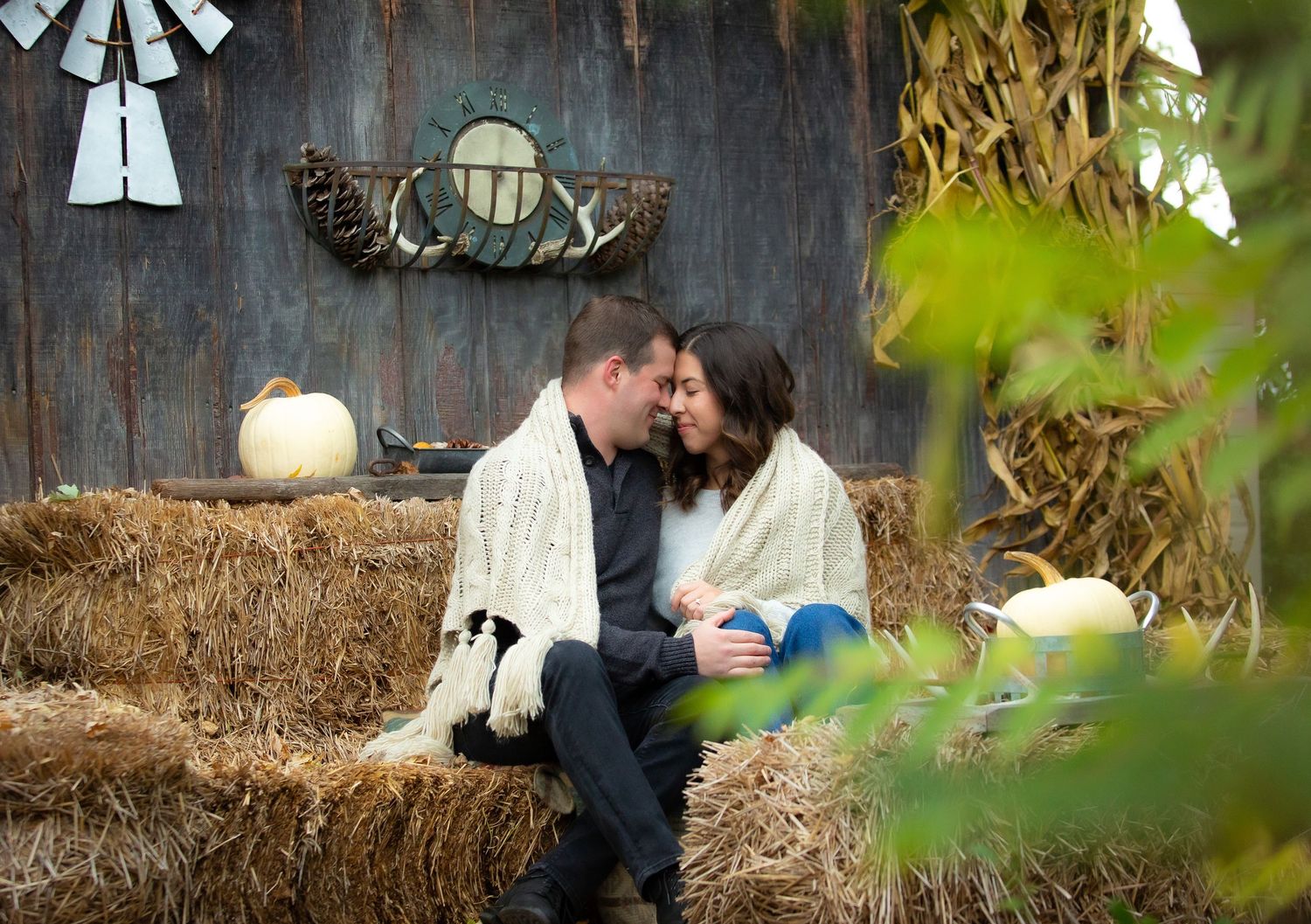 A romantic autumn scene with two people sitting close together on hay bales decorated with white pumpkins.