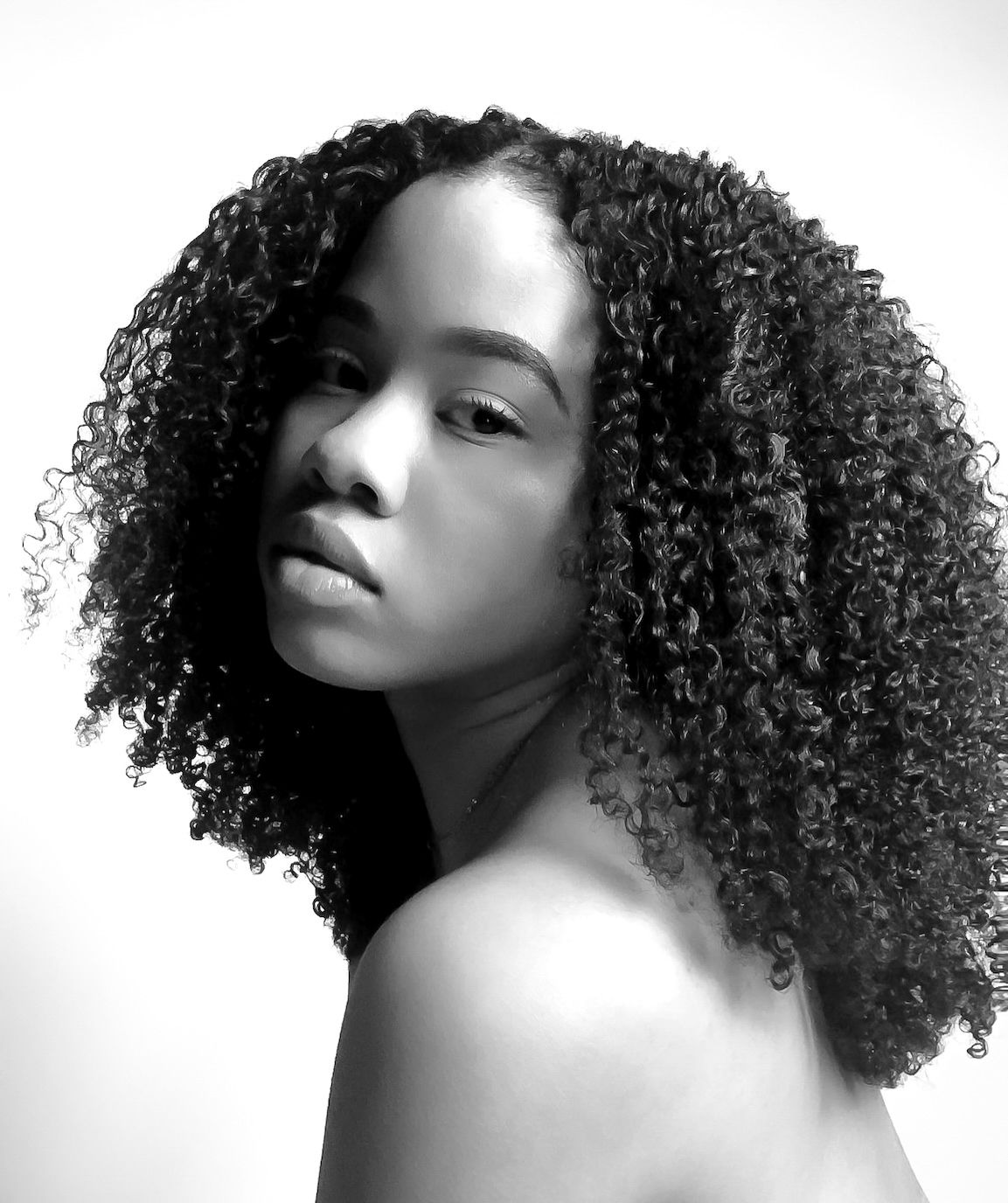 Black and white portrait of a young woman with voluminous curly hair, looking over her shoulder.