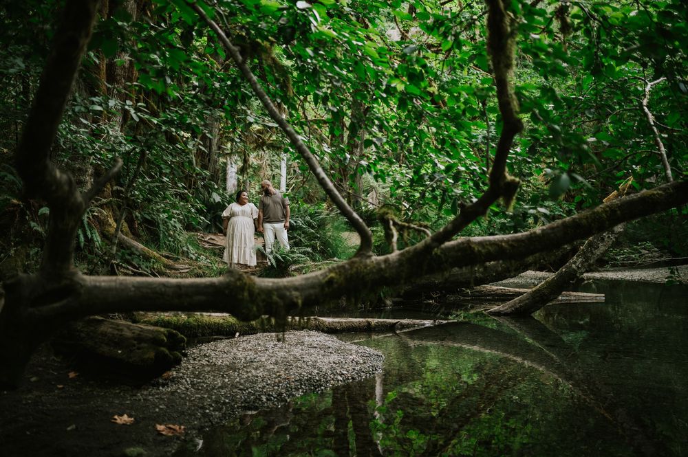 Photo of engaged couple standing in front of creek with reflection Cathedral Groves, MacMillan Park. Vancouver Island adventure photographer