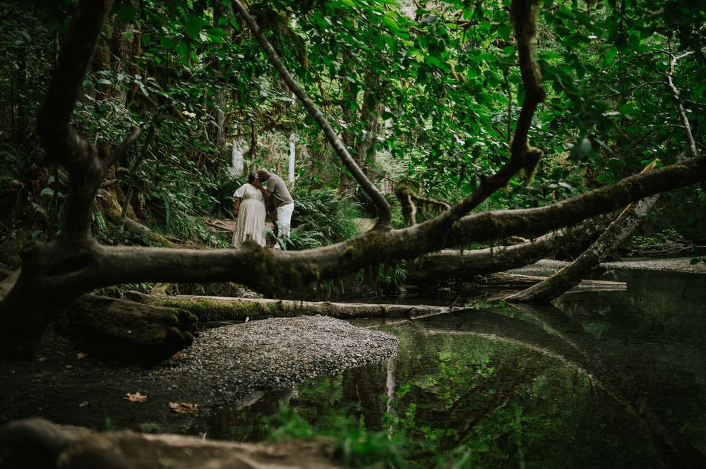 Portrait of engaged couple standing in front of creek in forest Cathedral Groves, MacMillan Park. Vancouver Island adventure photographer