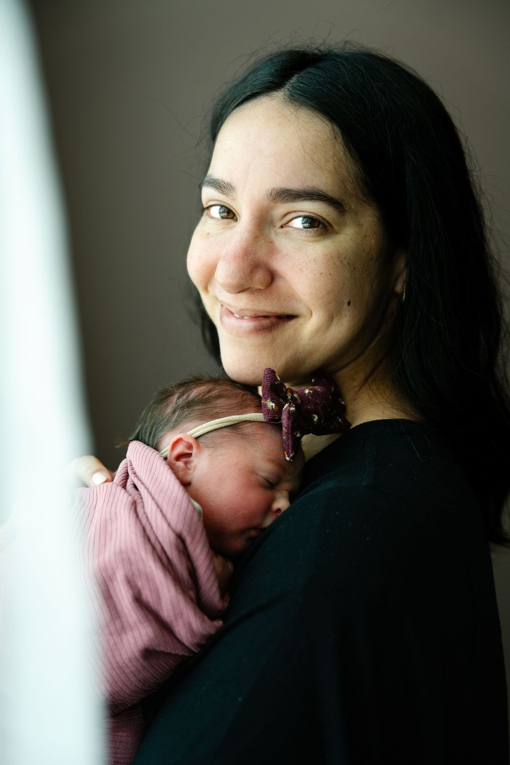 Sweet newborn baby sleeps peacefully against caregiver in soft pink wrapping.