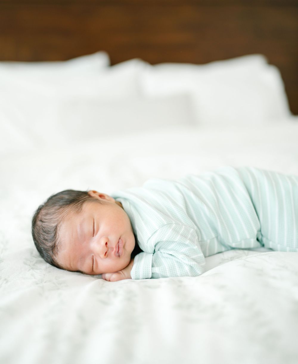 A peaceful newborn baby sleeps on white bedding wearing mint green.