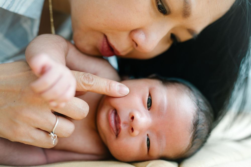 Mother and newborn sharing an intimate bonding moment on white bedding.