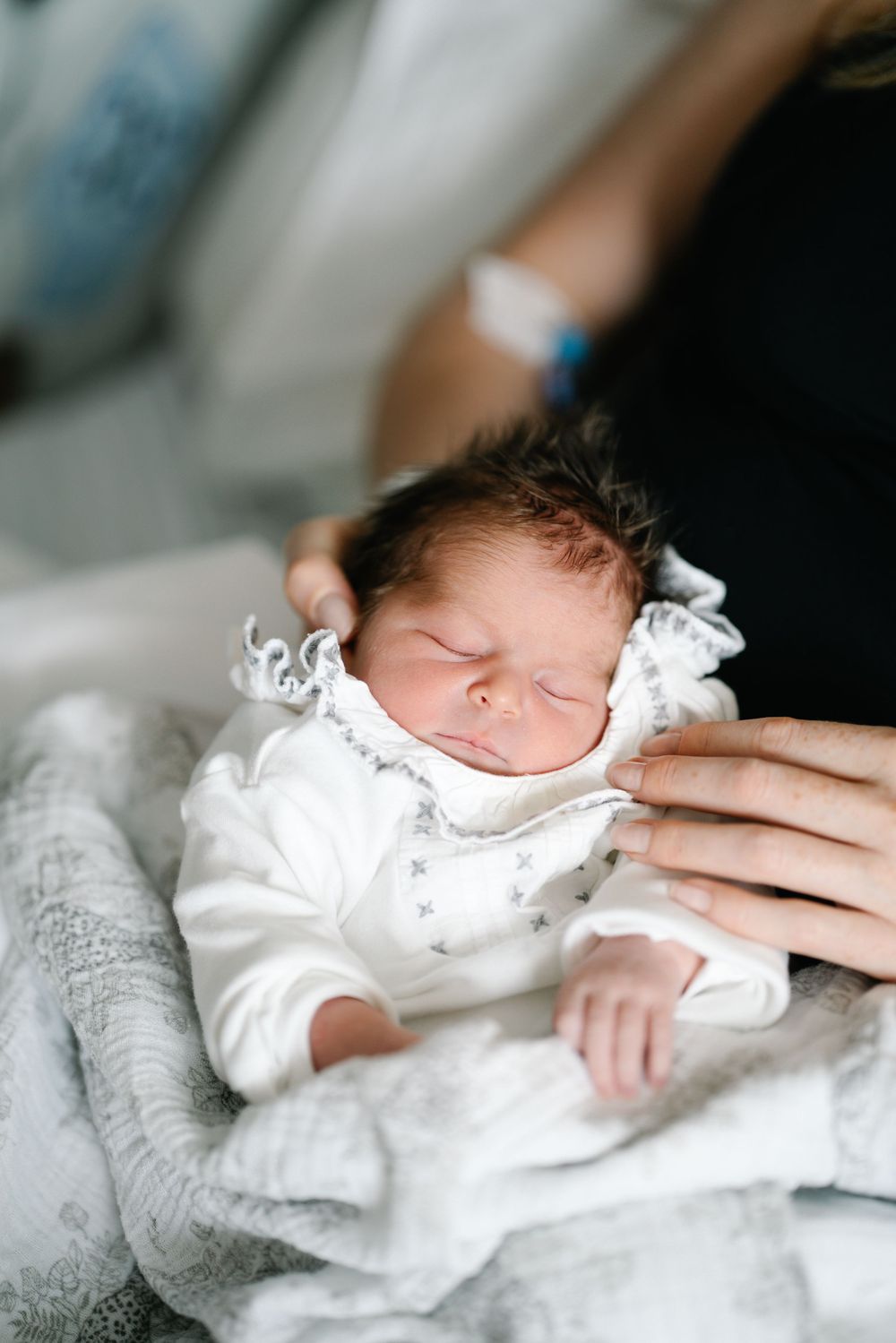 A sleeping newborn in white lace clothing resting on soft gray blankets.
