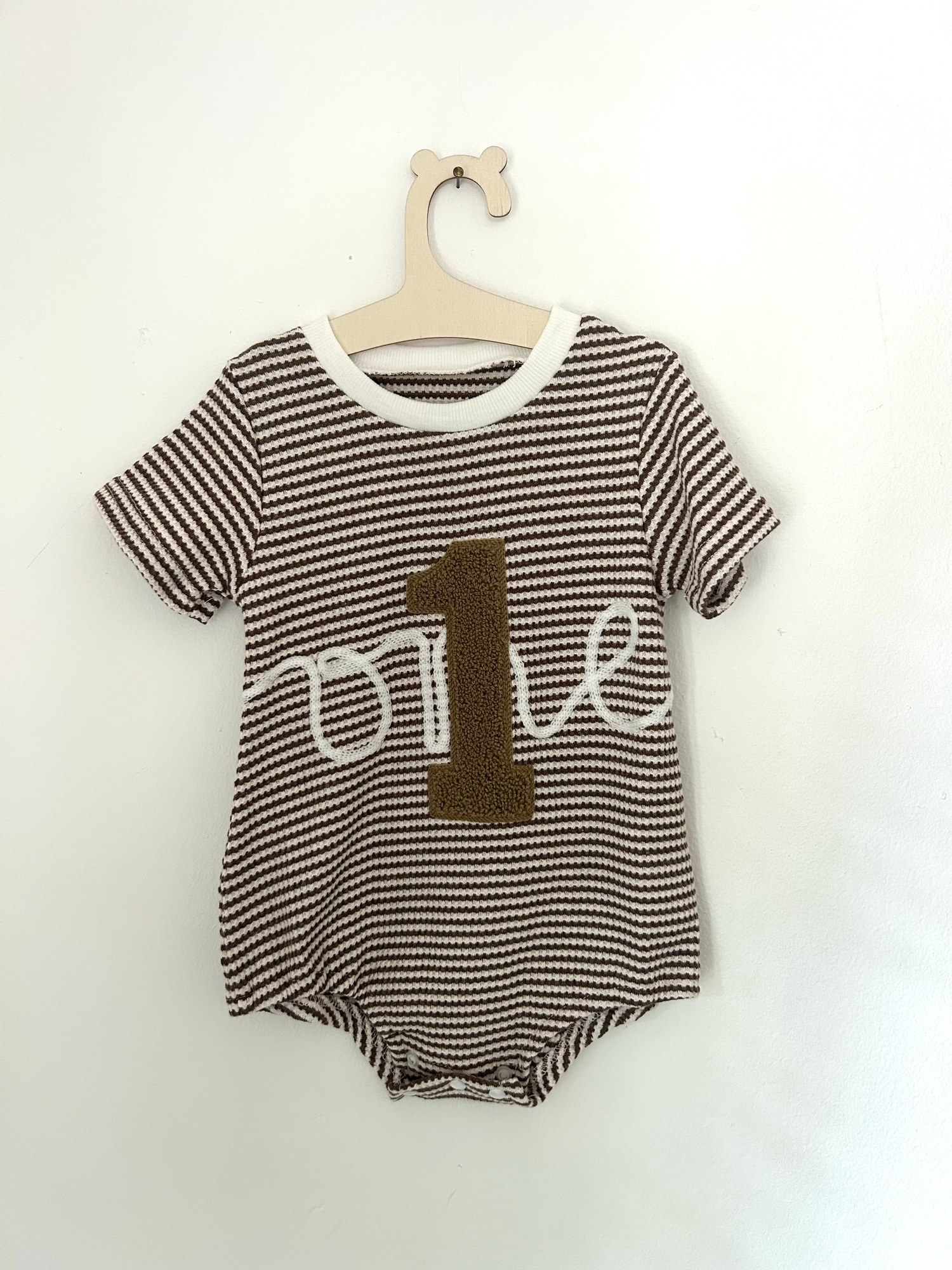 Vintage-style beige knitted baby romper with button details and side pockets hanging on display.